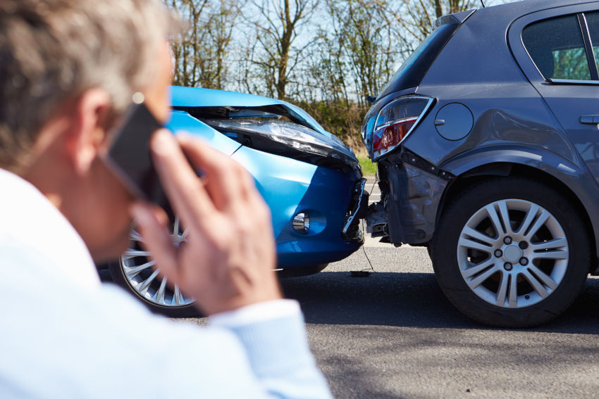 hombre de espaldas llamando por su teléfono móvil mientras observa los daños de dos coches que han tenido un accidente