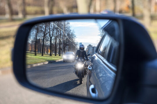 imagen desde el retrovisor derecho de un coche de una moto adelantando por la derecha