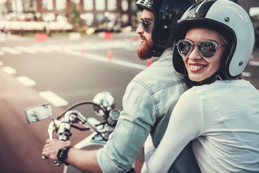 pareja joven sonriendo con gafas de soly casco jet de moto conduciendo un ciclomotor