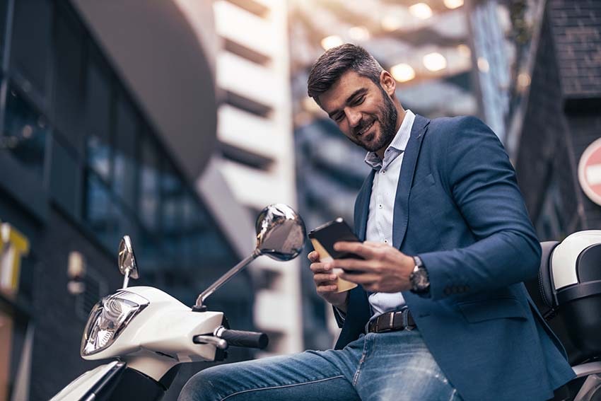 hombre sentado sobre una moto tipo scooter mirando la pantalla de su teléfono