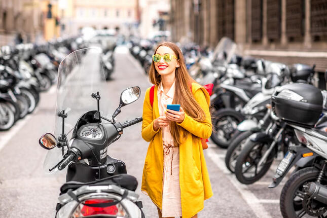chica vestida de amarillo al lado de un scooter con el móvil en la mano