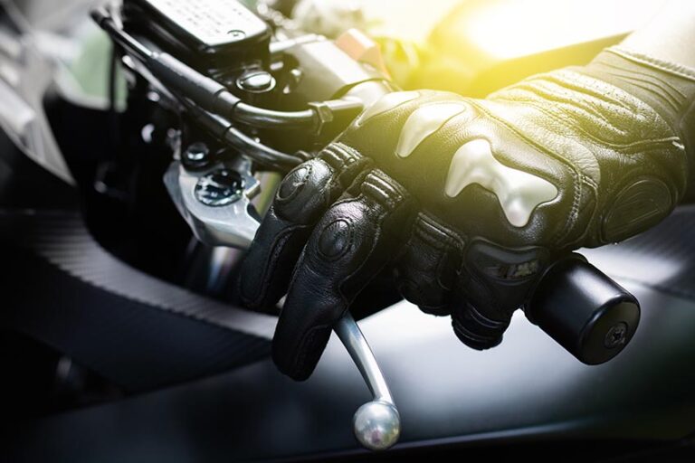 Primer plano de la mano de un motorista con guantes de protección agarrando la palanca de embrague de la moto