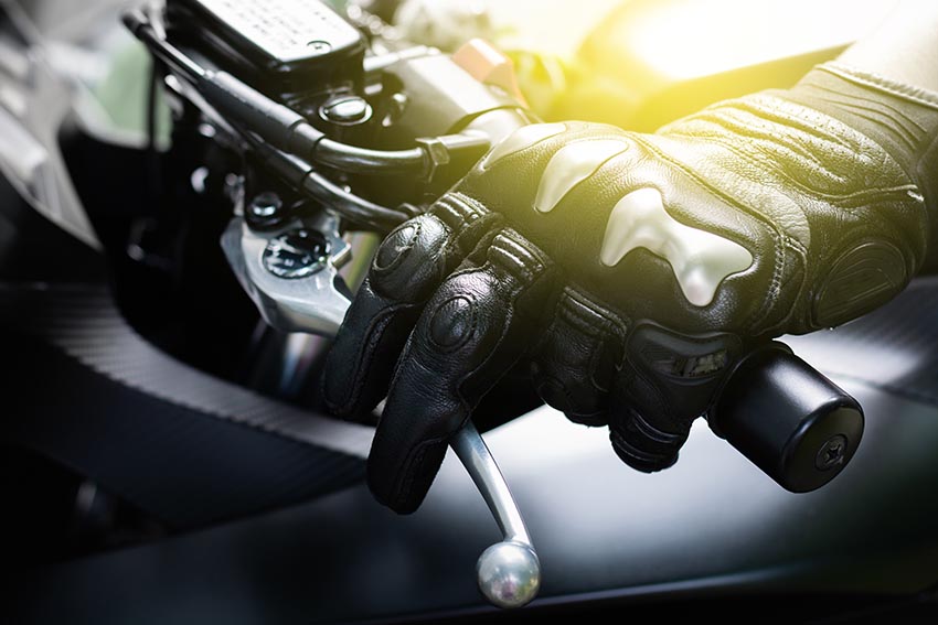 Primer plano de la mano de un motorista con guantes de protección agarrando la palanca de embrague de la moto,