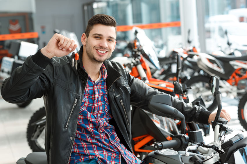 hombre joven sentado en una moto  nueva y mostrando las llaves en un concesionario 