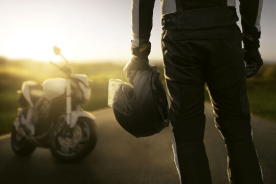 motorista de espaldas con casco de moto en su mano mirando hacia su moto