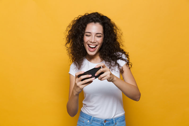mujer joven sonriendo miestras juega con el móvil