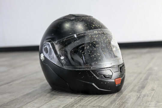 casco de moto integral de color negro con salpicaduras de barro y apoyado sobre el suelo