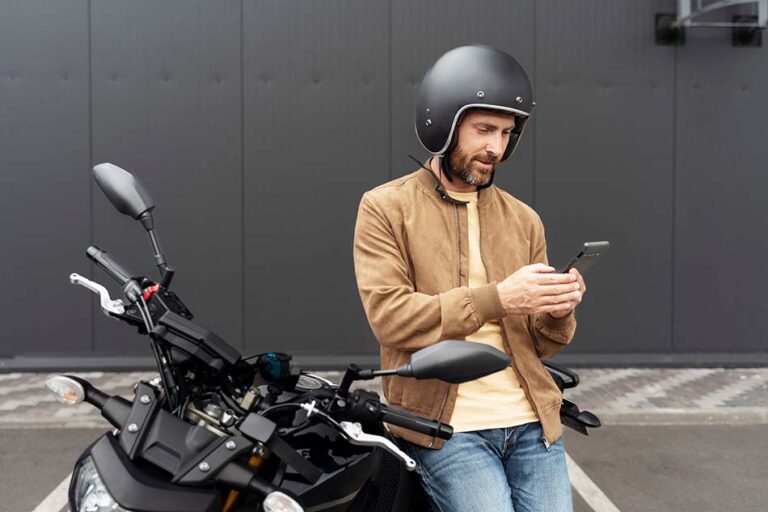 hombre apoyado sobre el lateral de su moto con el teléfono móvil en las manos