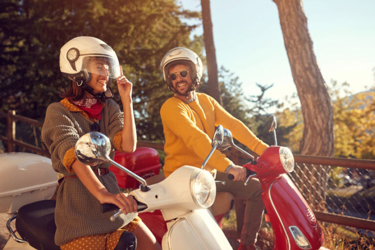 una motera y un motero riendo montados en sus scooters.