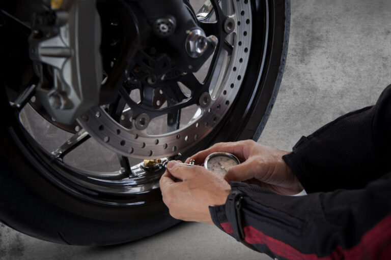 primer plano de las manos de un hombre midiendo la presión de los neumáticos de la rueda delantera de una moto
