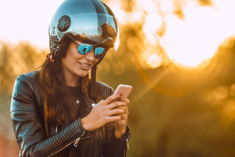 mujer con casco y chaqueta moteros con un smartphone en la mano