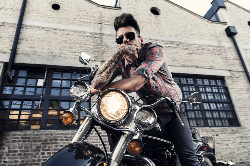 Joven sentado en su moto apoyando sus brazos tatuados en el manillar