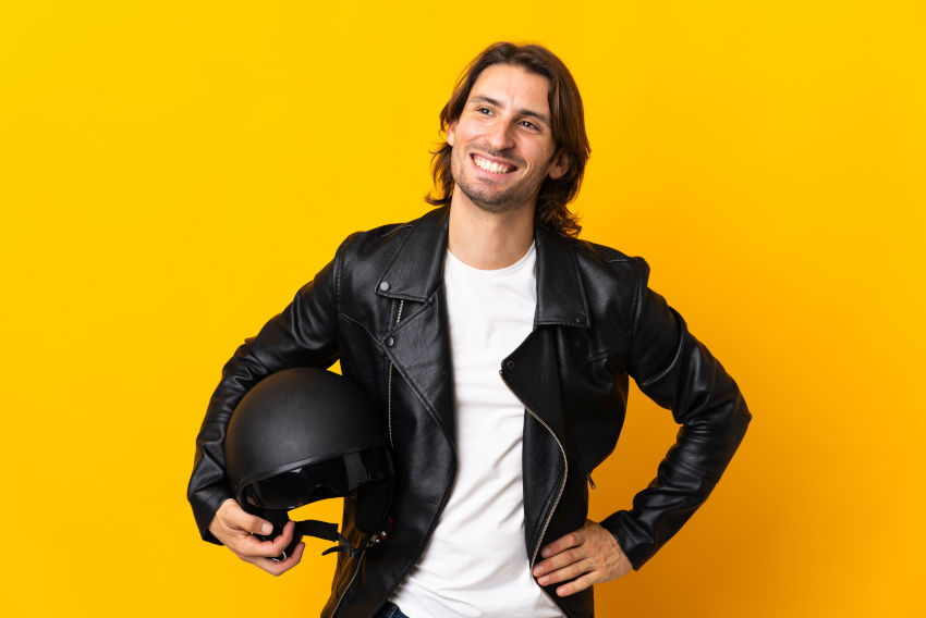 hombre joven sonriente con chaqueta de cuero y sujetando un casco con el brazo derecho